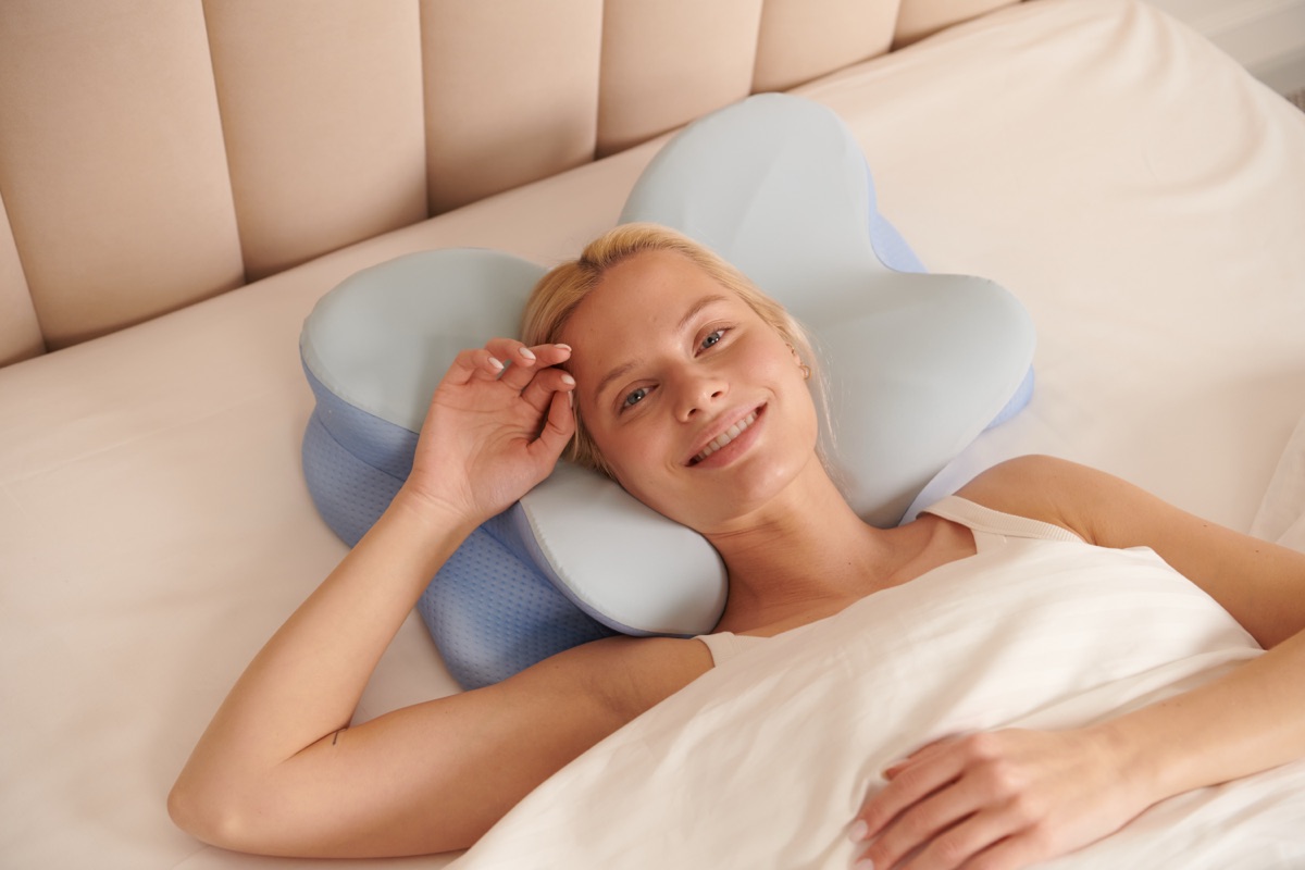 Woman sleeping comfortably on an ergonomic contour pillow, smiling